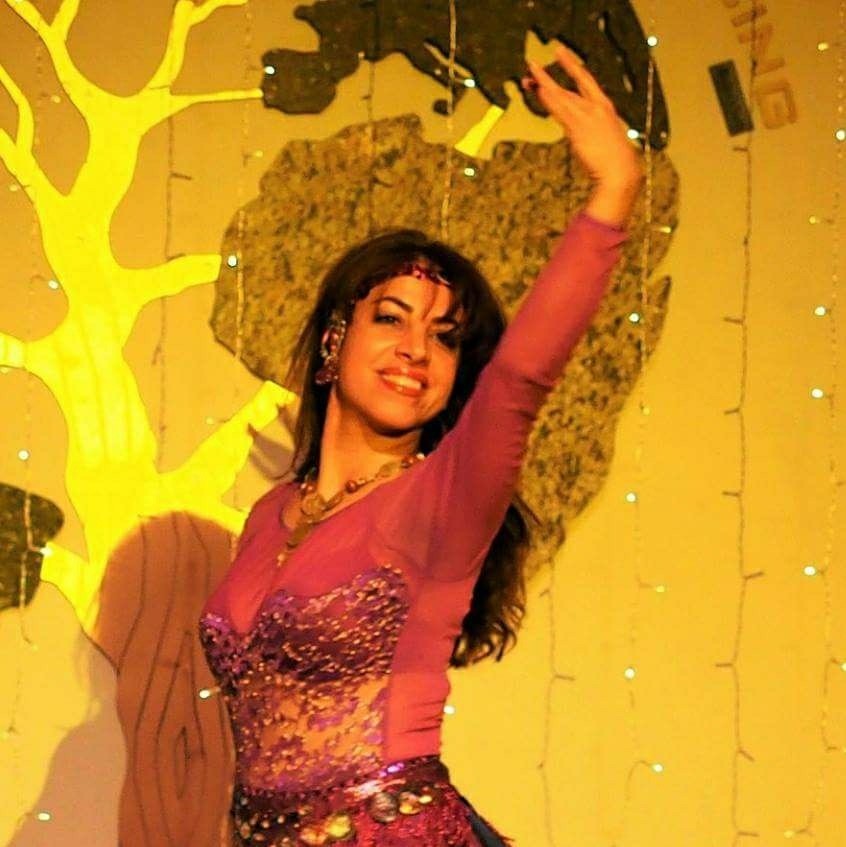 Elham performing wearing an embellished pink dress in front of a golden colored backdrop